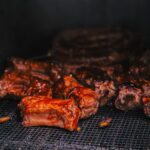 Ant grotelių kepami sultingi kiaulienos šonkauliukai, padengti blizgiu barbekiu padažu.