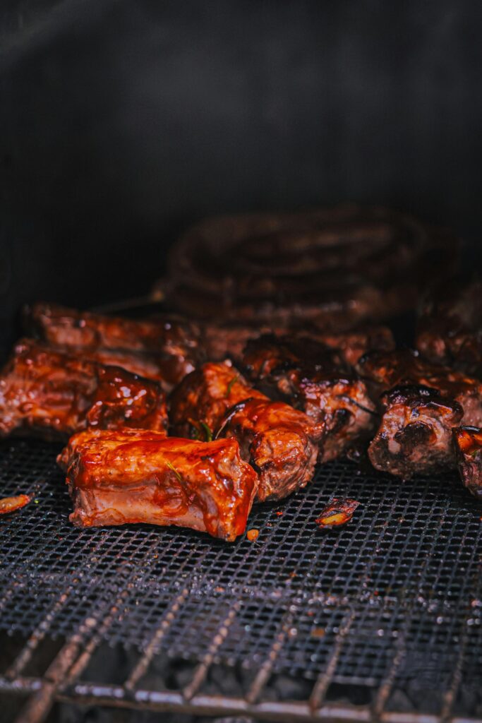Ant grotelių kepami sultingi kiaulienos šonkauliukai, padengti blizgiu barbekiu padažu.
