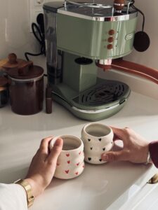 Besišypsanti šeima leidžianti laiką šviesioje virtuvėje prie modernaus kavos aparato.