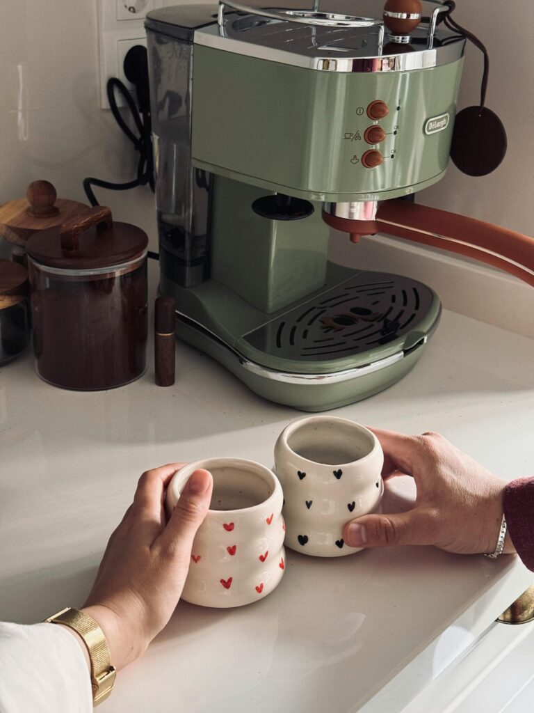 Besišypsanti šeima leidžianti laiką šviesioje virtuvėje prie modernaus kavos aparato.