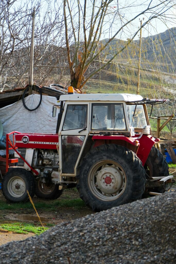 Siauresnių ratų mini traktorius dirba sename obelų sode.